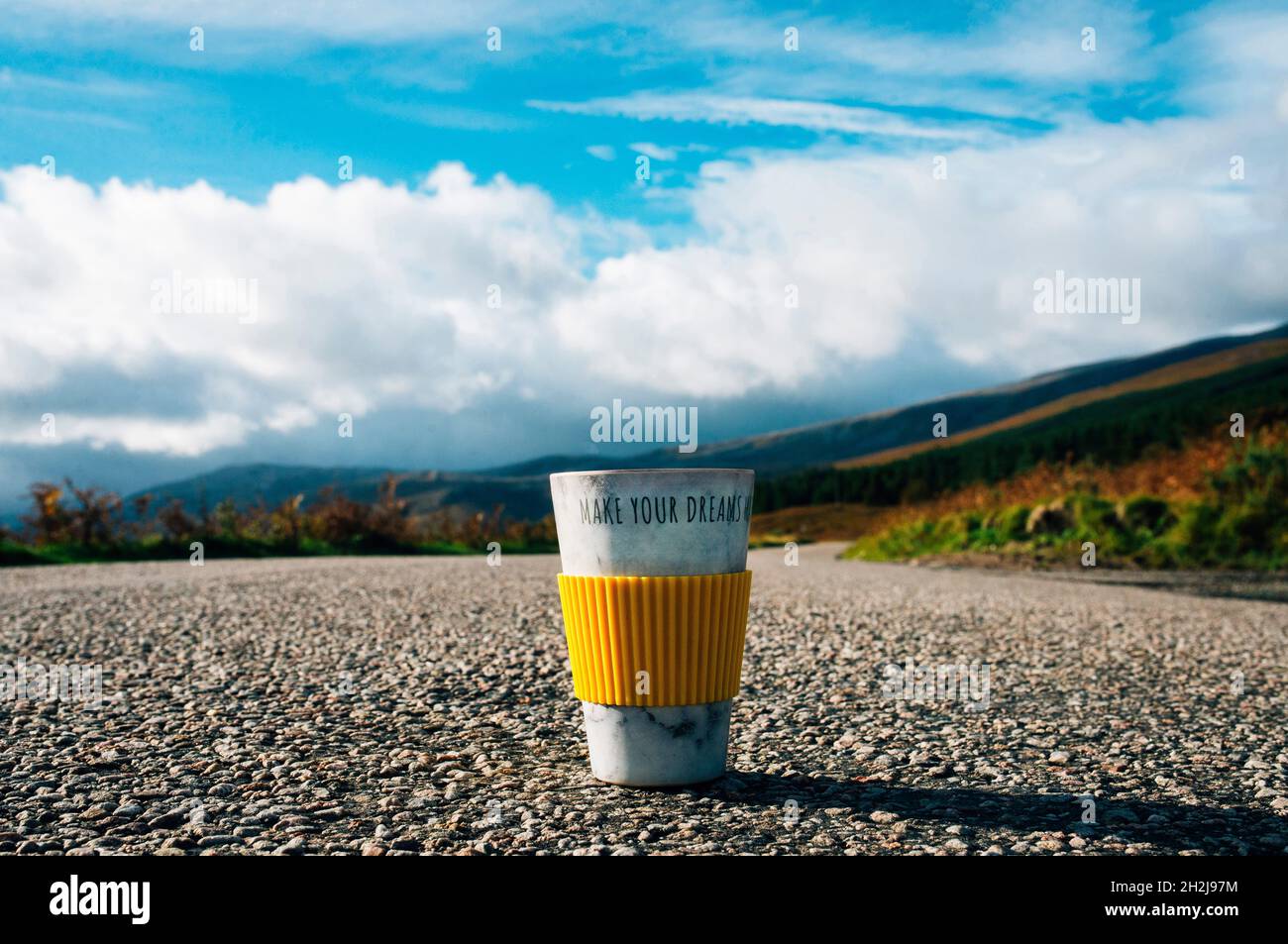 une tasse de voyage avec les mots font vos rêves sur elle.Route ouverte et montagnes en arrière-plan.Suivez vos rêves.Source d'inspiration Banque D'Images