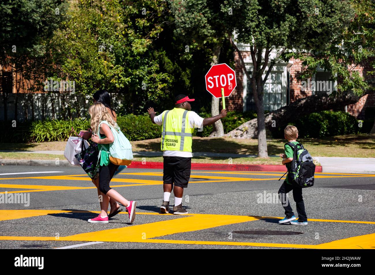 Les enfants des écoles traversent une rue animée avec l'aide d'un garde-passage Banque D'Images