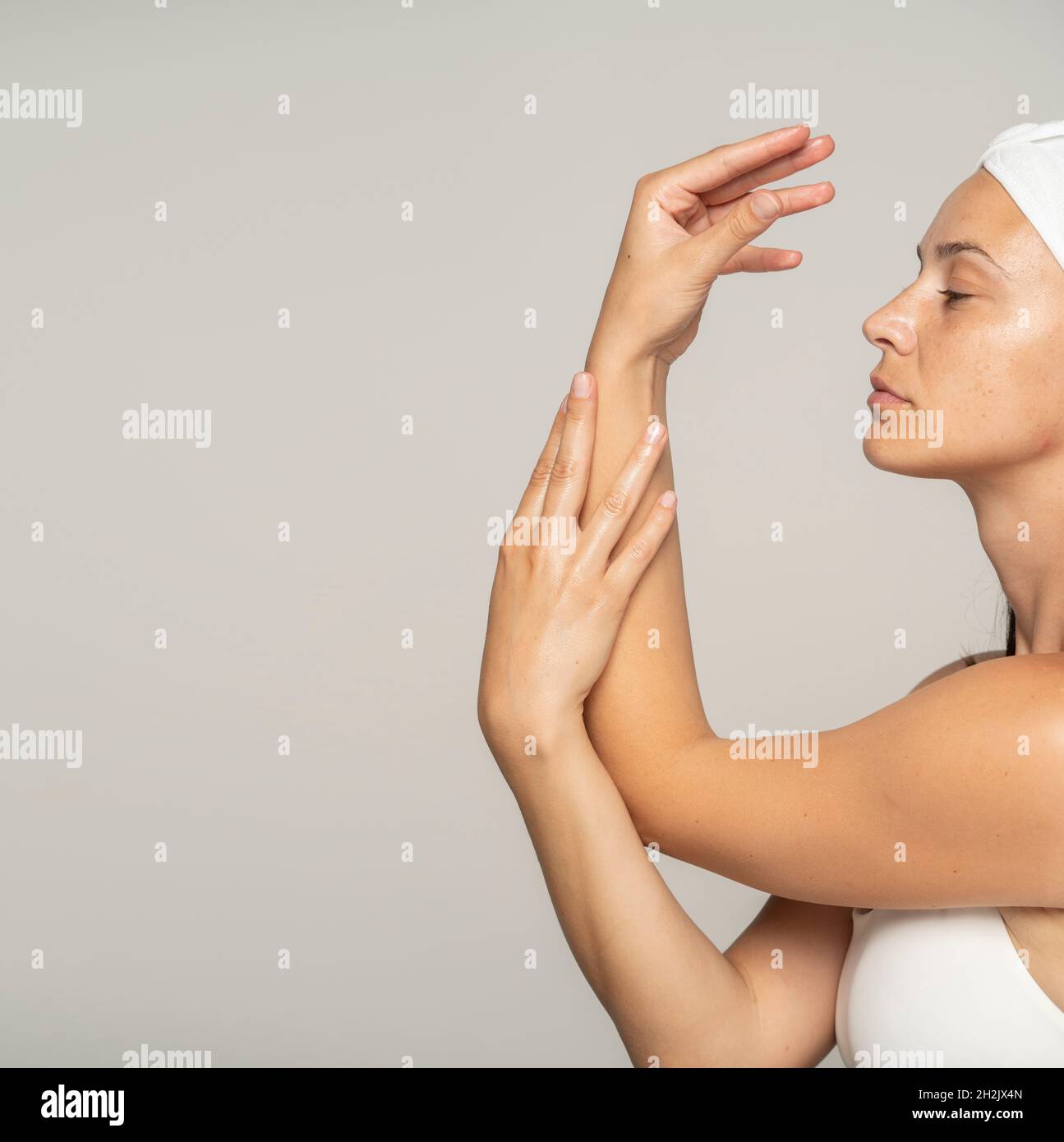une jeune belle femme applique un produit cosmétique sur ses mains sur un fond gris Banque D'Images
