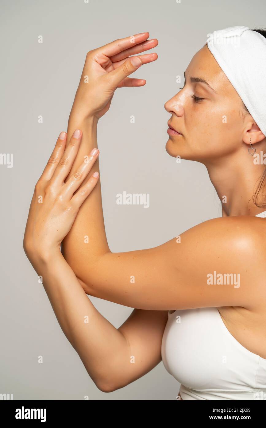 une jeune belle femme applique un produit cosmétique sur ses mains sur un fond gris Banque D'Images