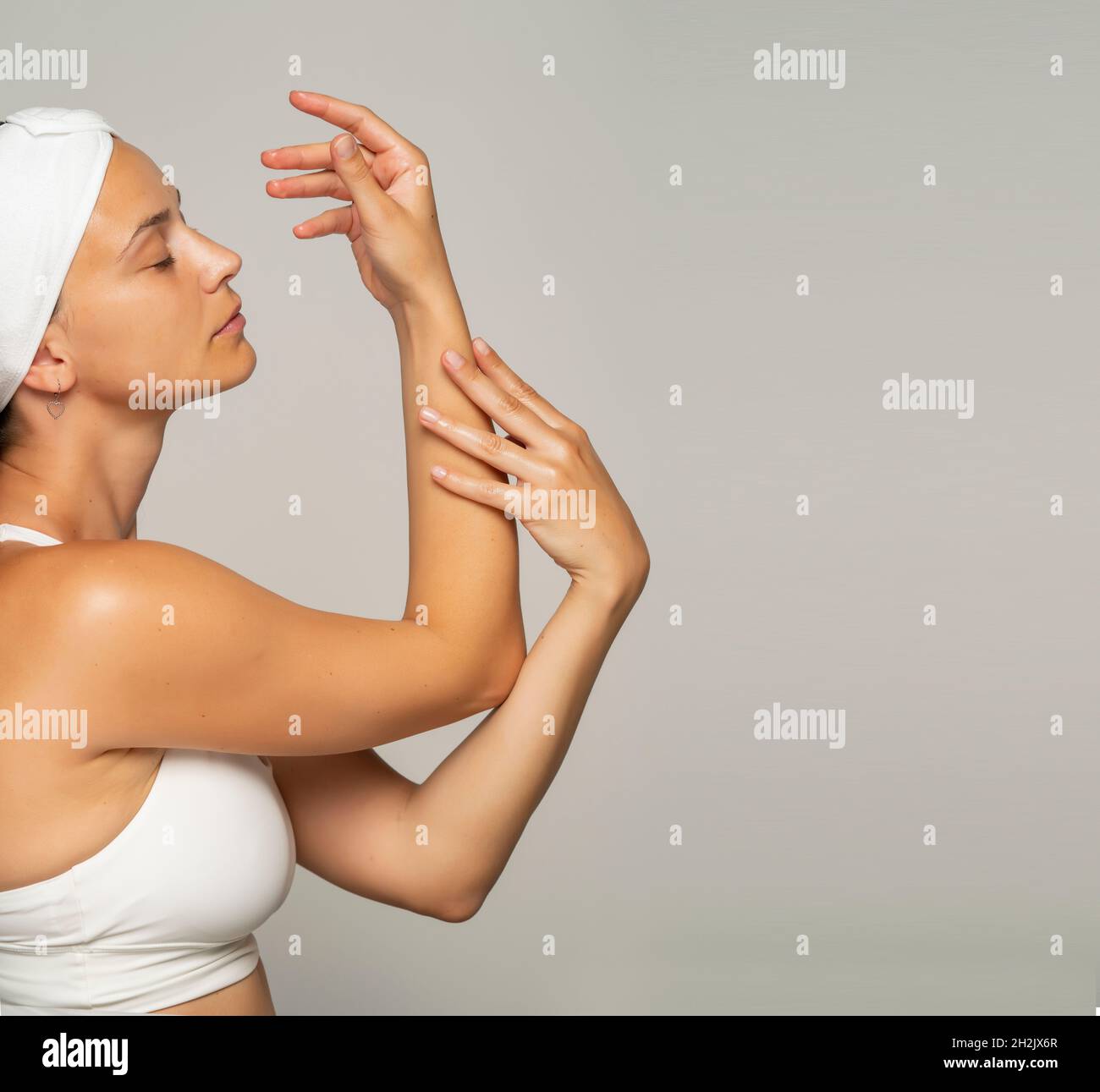 une jeune belle femme applique un produit cosmétique sur ses mains sur un fond gris Banque D'Images