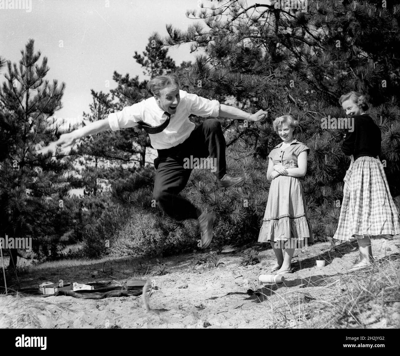 Jeune homme impressant les filles en sautant dans l'air Grande-Bretagne 1950 Banque D'Images