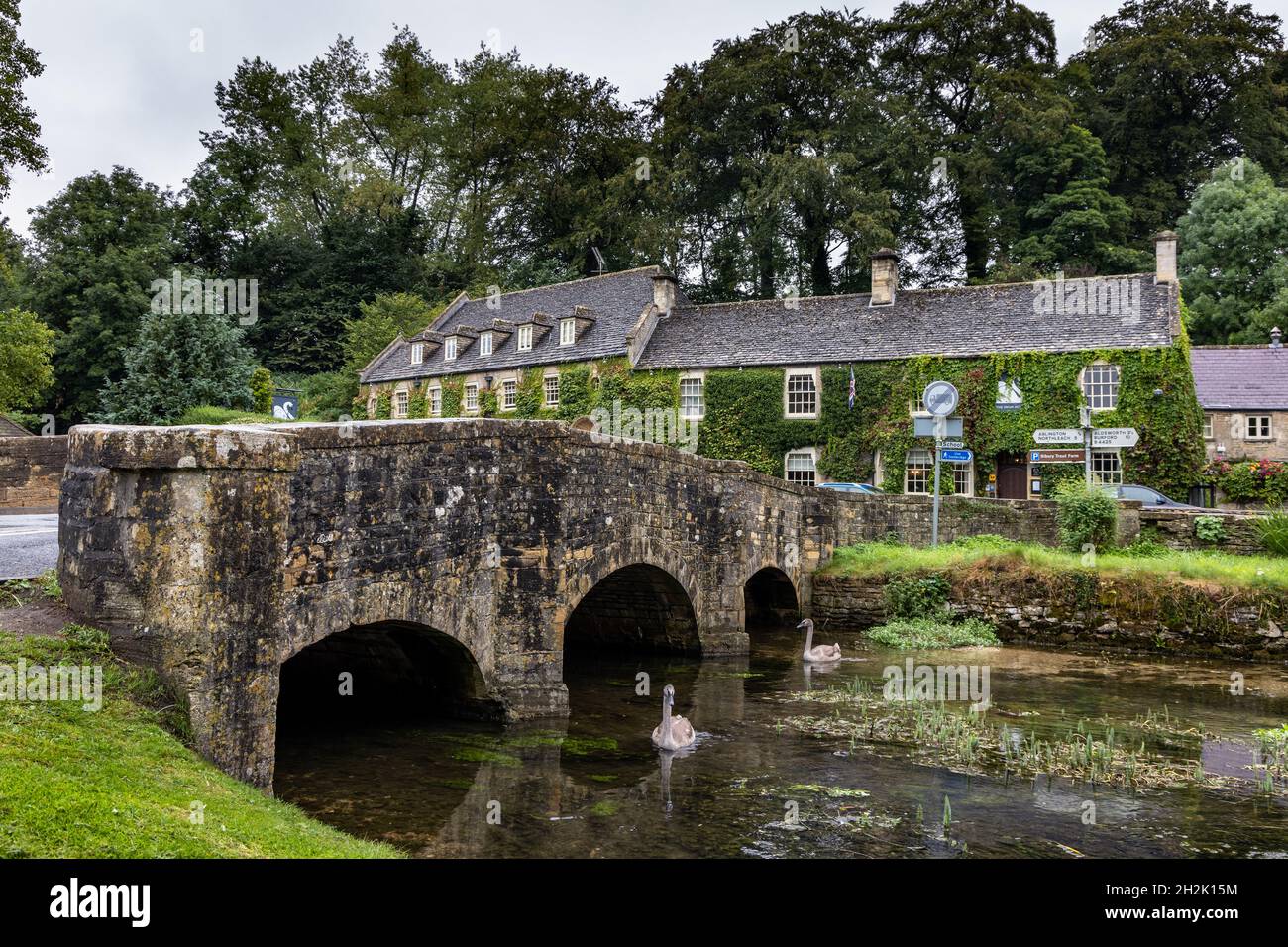 Le pont en pierre sur la rivière Coln et l'ivy Covered Swan Hotel dans le village pittoresque de Bibury, dans les Cotswolds du Gloucestershire, en Angleterre. Banque D'Images