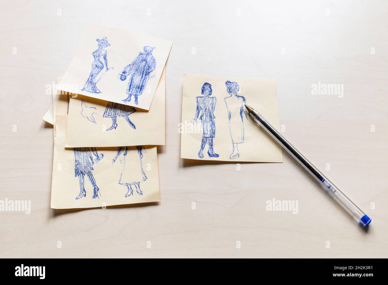 Croquis de la silhouette à la mode de la femme du XX siècle dessiné à la main par un stylo bleu sur des feuilles de papier sur une table marron clair Banque D'Images