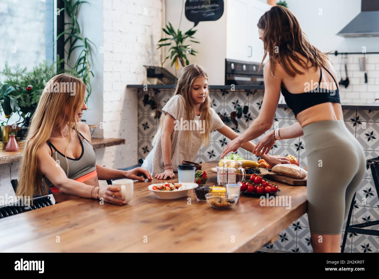 Des amies et une petite sœur font un repas léger de légumes, de fruits et de salade pour un en-cas post-entraînement Banque D'Images