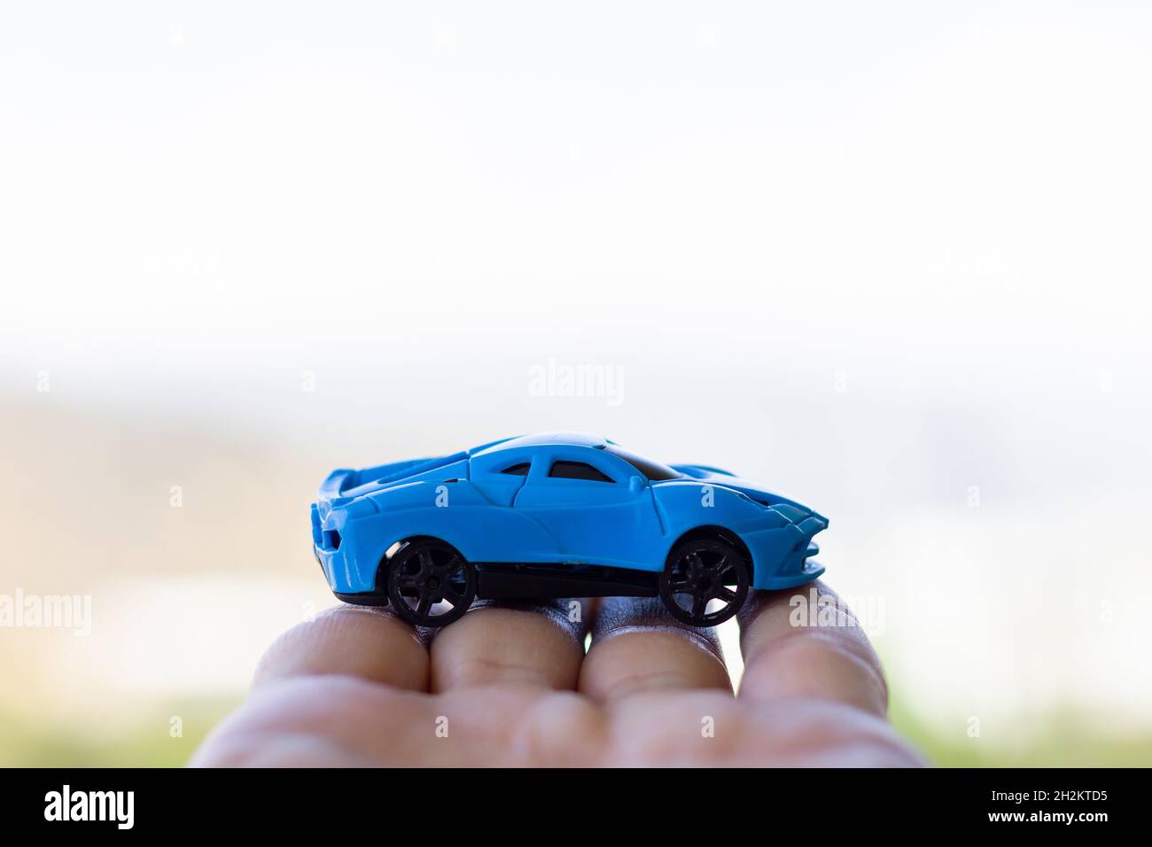 Main tenant sport bleu jouet voiture sur fond blanc flou Banque D'Images