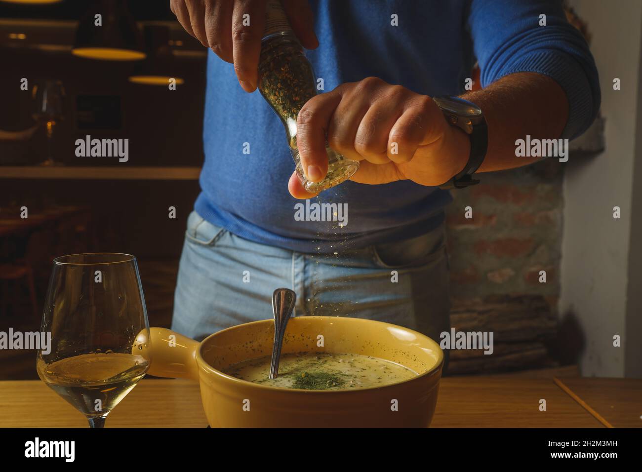 Vue de face gros plan sur les mains d'un inconnu ajoutant du poivre ou d'autres épices au fromage fondu dans un bol sur la table pour préparer des aliments Banque D'Images