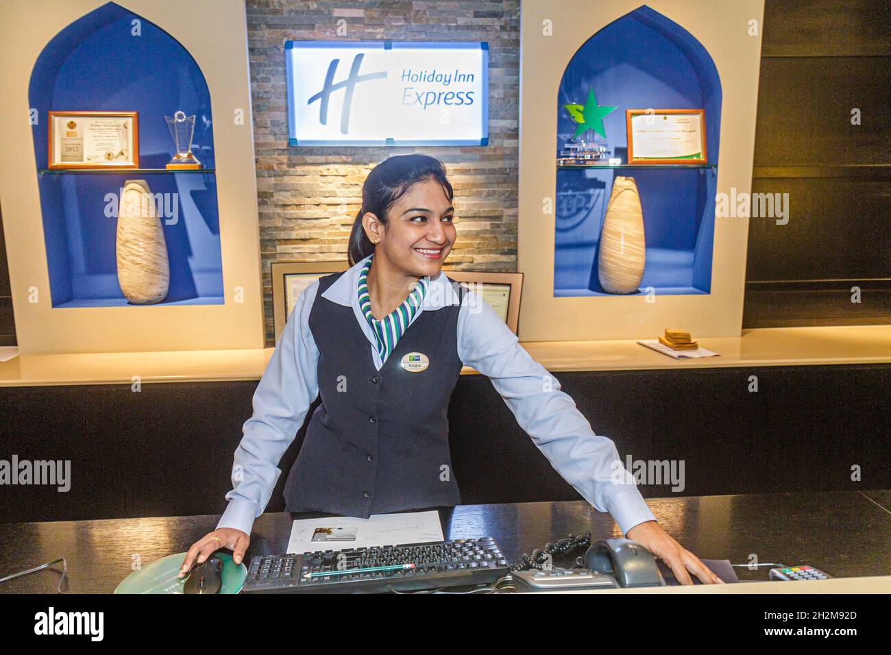 Dubai eau, Garhoud, Holiday Inn Express hall de l'hôtel, femme musulmane réception, enregistrement à la réception réservations personnel souriant employé à l'intérieur Banque D'Images