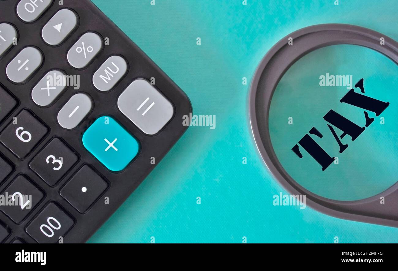 Taxe sur la loupe, à côté d'une calculatrice sur fond turquoise Banque D'Images