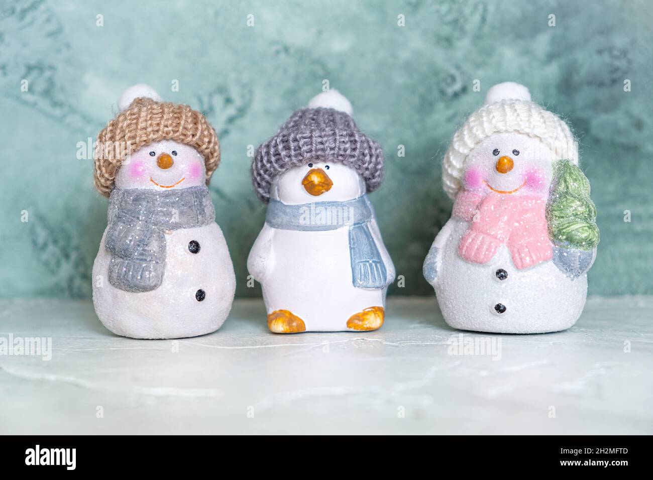 Trois jouets en céramique du nouvel an - un pingouin et des bonhommes de neige en chapeaux tricotés et foulards sur fond turquoise.Concept nouvel an et noël.Salutation Banque D'Images