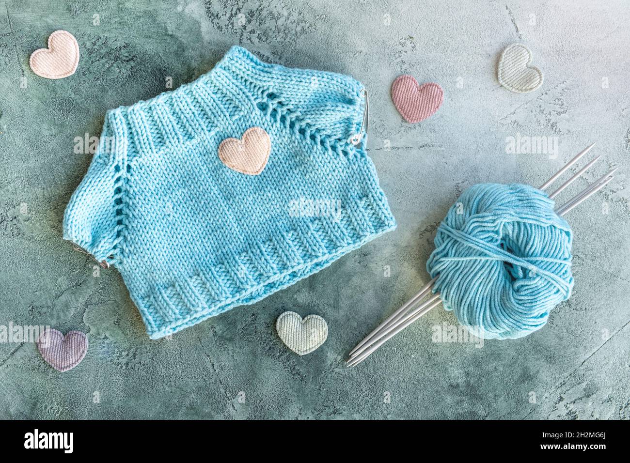 Le concept de tricotage des vêtements pour les jouets et les bébés.T-shirt tricoté en fil de coton turquoise.Une boule de fil, aiguilles de tricotage et velours Banque D'Images