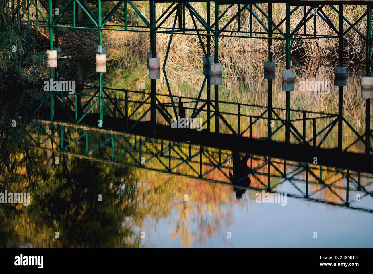 Réflexion dans l'eau de personnes marchant sur un pont piétonnier dans un parc pendant une journée d'automne ensoleillée. Banque D'Images