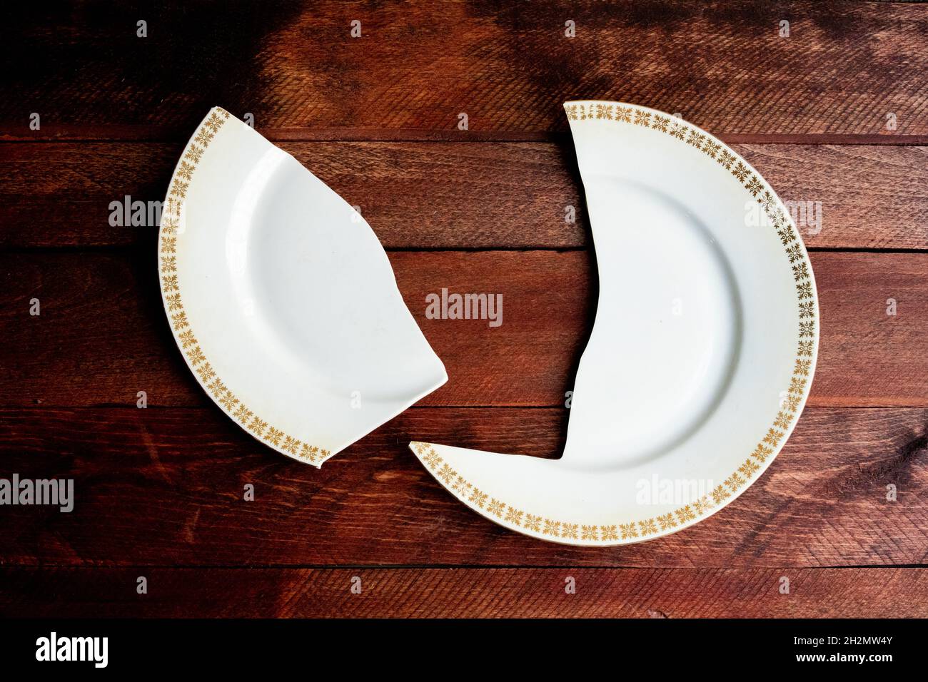 Assiette en porcelaine blanche brisée simple avec cadre doré sur une terrasse en bois rouge Banque D'Images