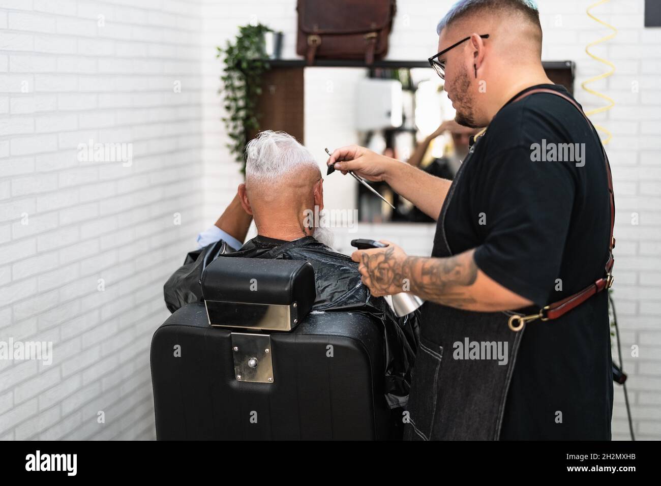 Coiffeur masculin coupant les cheveux à la barbe client senior - jeune coiffeur travaillant dans le barbershop - concept de salon de soins de santé et de coupe de cheveux Banque D'Images