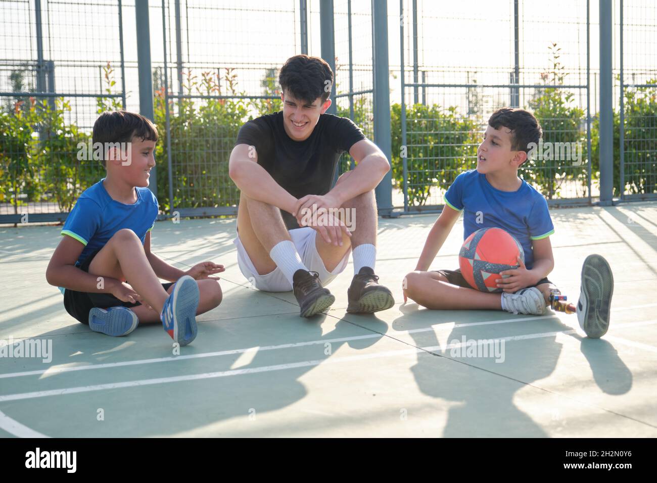 Trois frères assis sur le sol du terrain de football se reposant et parlant. Banque D'Images