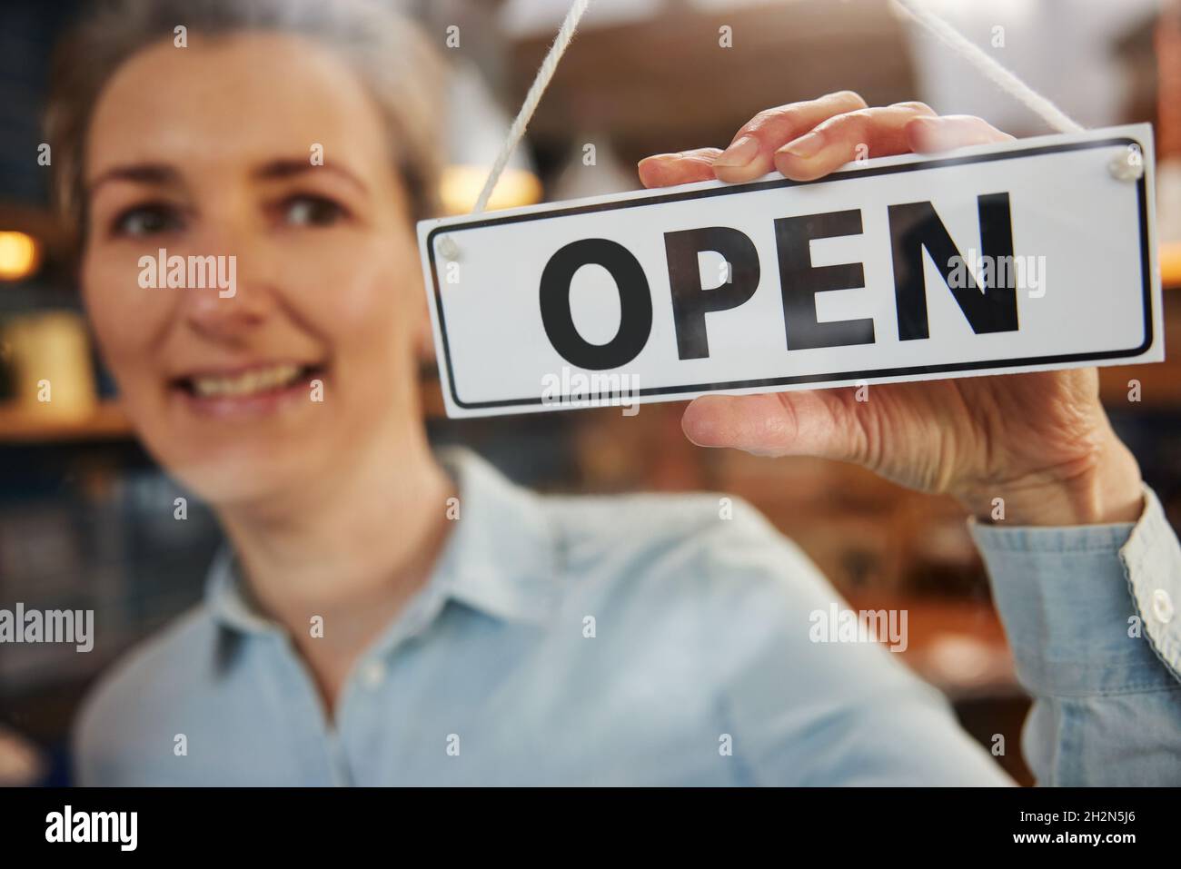 Femme propriétaire d'une petite entreprise tournant l'affiche ronde ouverte sur la porte Banque D'Images