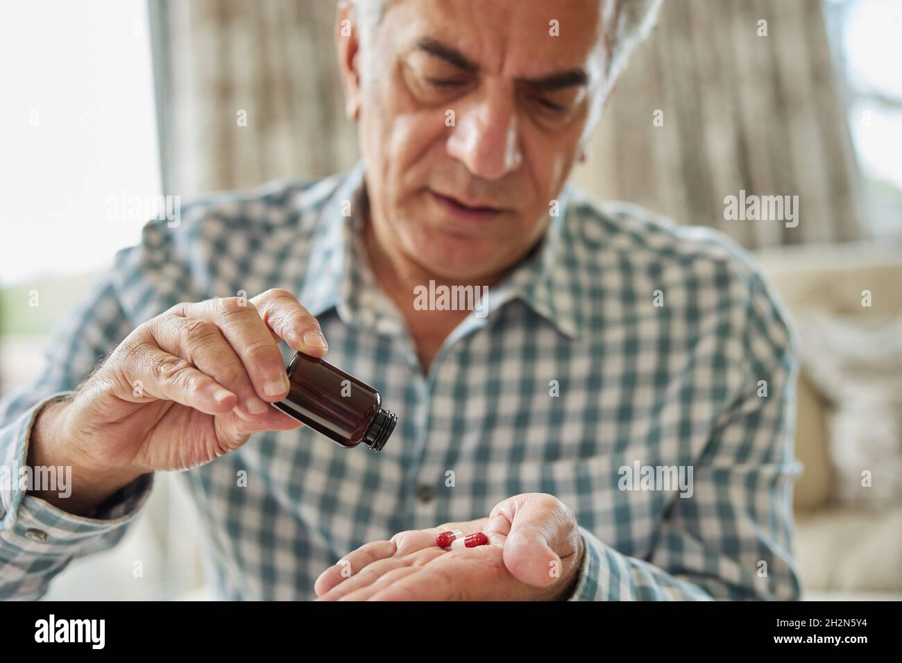 Homme mature assis sur un canapé à la maison prenant des pilules de médicament de la bouteille Banque D'Images