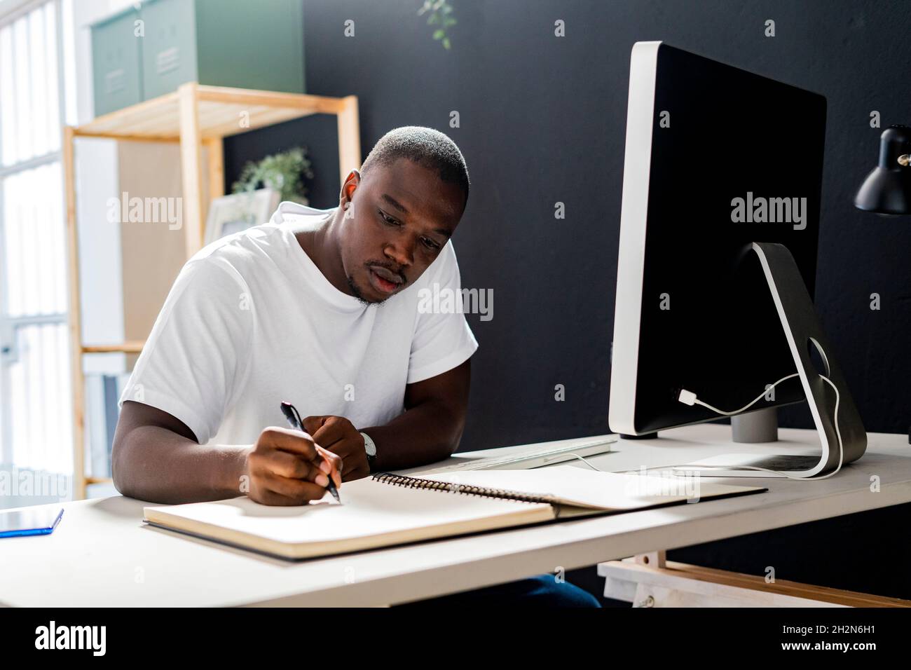 Travailleur indépendant de sexe masculin, main sur le menton, regardant un ordinateur de bureau en studio Banque D'Images