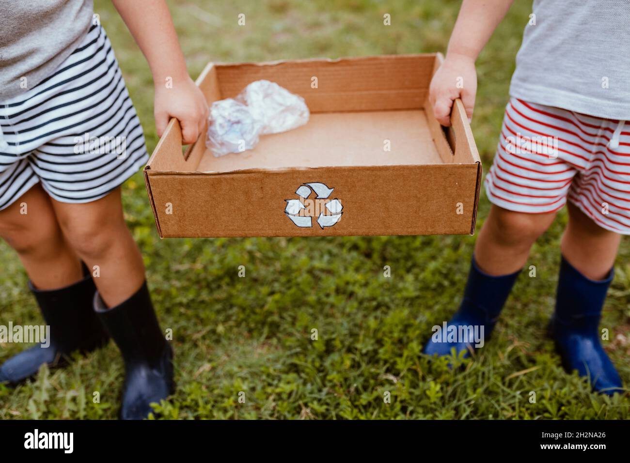 Les garçons collectent le plastique dans une boîte en carton avec le symbole de recyclage Banque D'Images