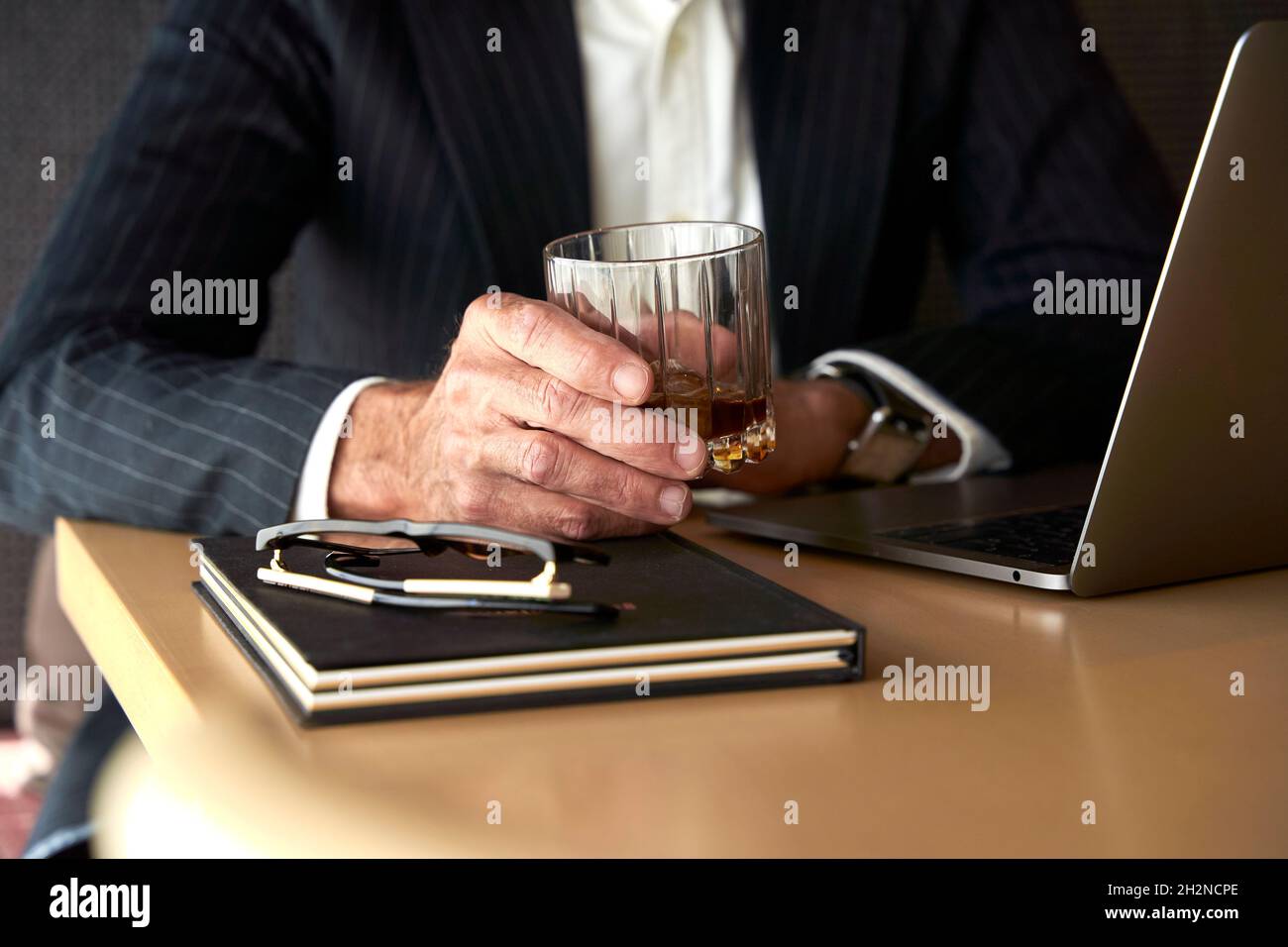 Homme d'affaires mature tenant un verre à whisky par ordinateur portable à l'hôtel Banque D'Images