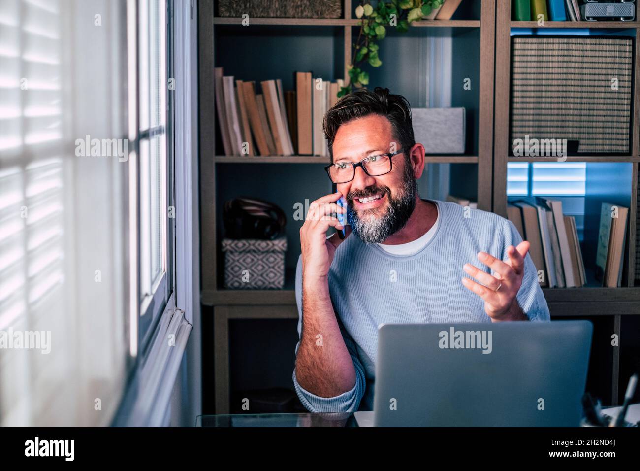 Un travailleur indépendant qui fait des gestes tout en parlant sur un téléphone intelligent au bureau à domicile Banque D'Images