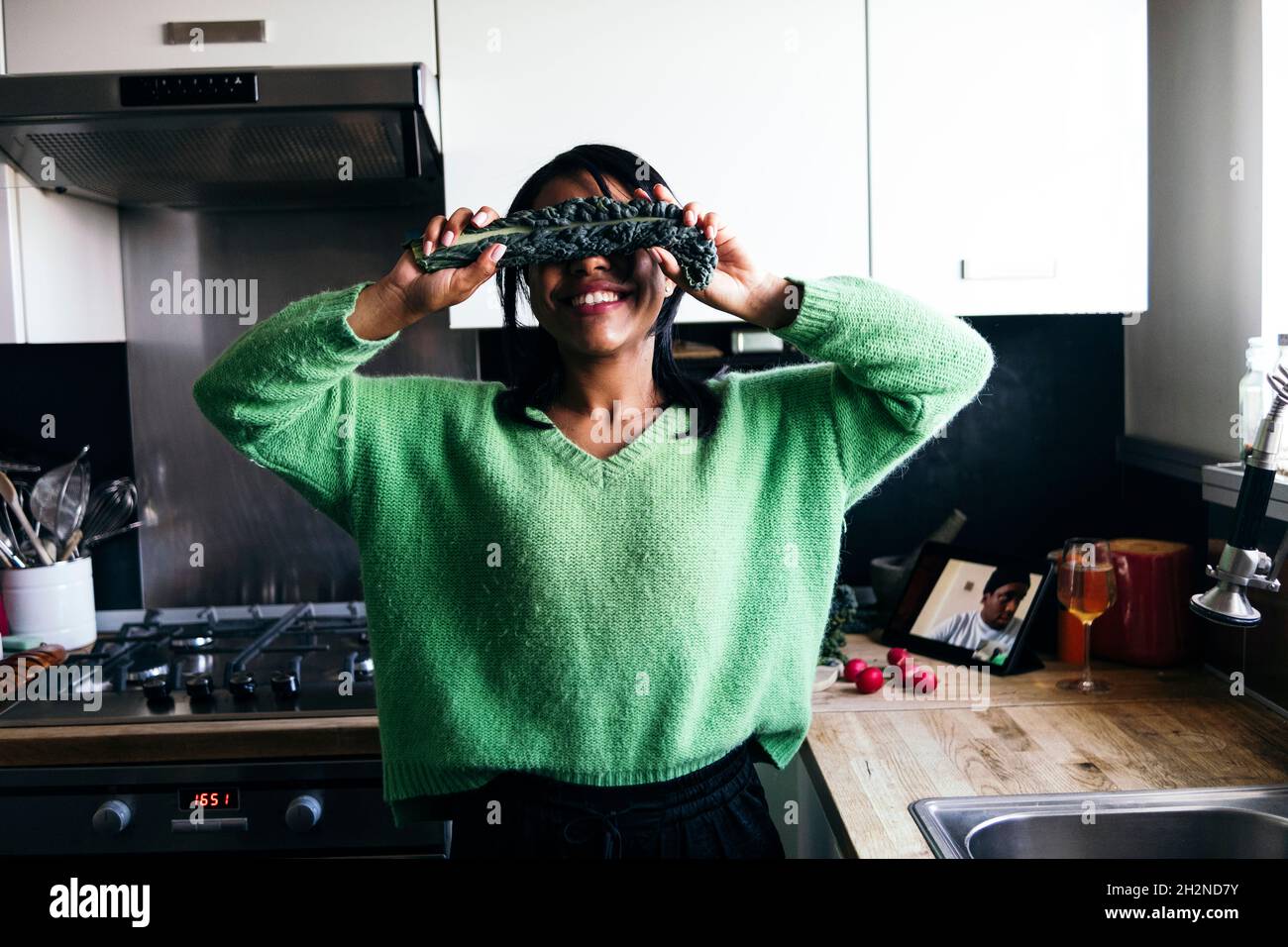 Femme souriante couvrant les yeux avec du kale dans la cuisine à la maison Banque D'Images