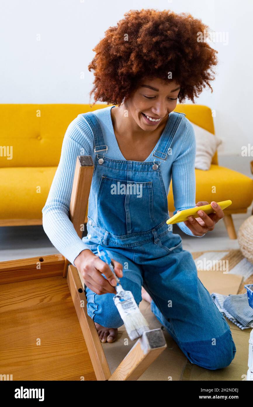 REDHEAD Afro femme avec une vieille chaise utilisant un smartphone à la maison Banque D'Images