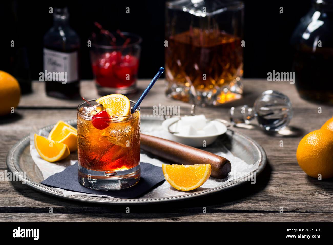 Cocktail à l'ancienne dans le verre Rocks avec ingrédients et outils de bar dans le bar en bois d'époque sombre Banque D'Images