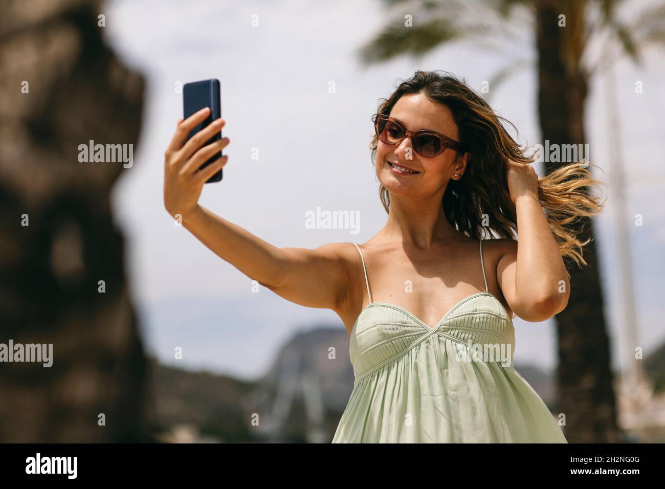 Femme adulte de taille moyenne avec main dans les cheveux prenant le selfie à travers le smartphone Banque D'Images