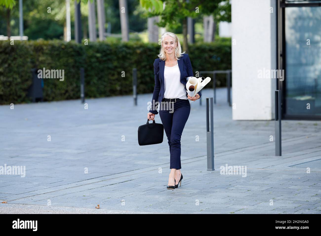 Femme d'affaires avec des plans et un sac d'ordinateur portable marchant sur le sentier Banque D'Images
