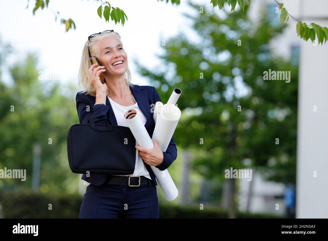 Femme d'affaires souriante tenant des plans tout en parlant sur un smartphone Banque D'Images