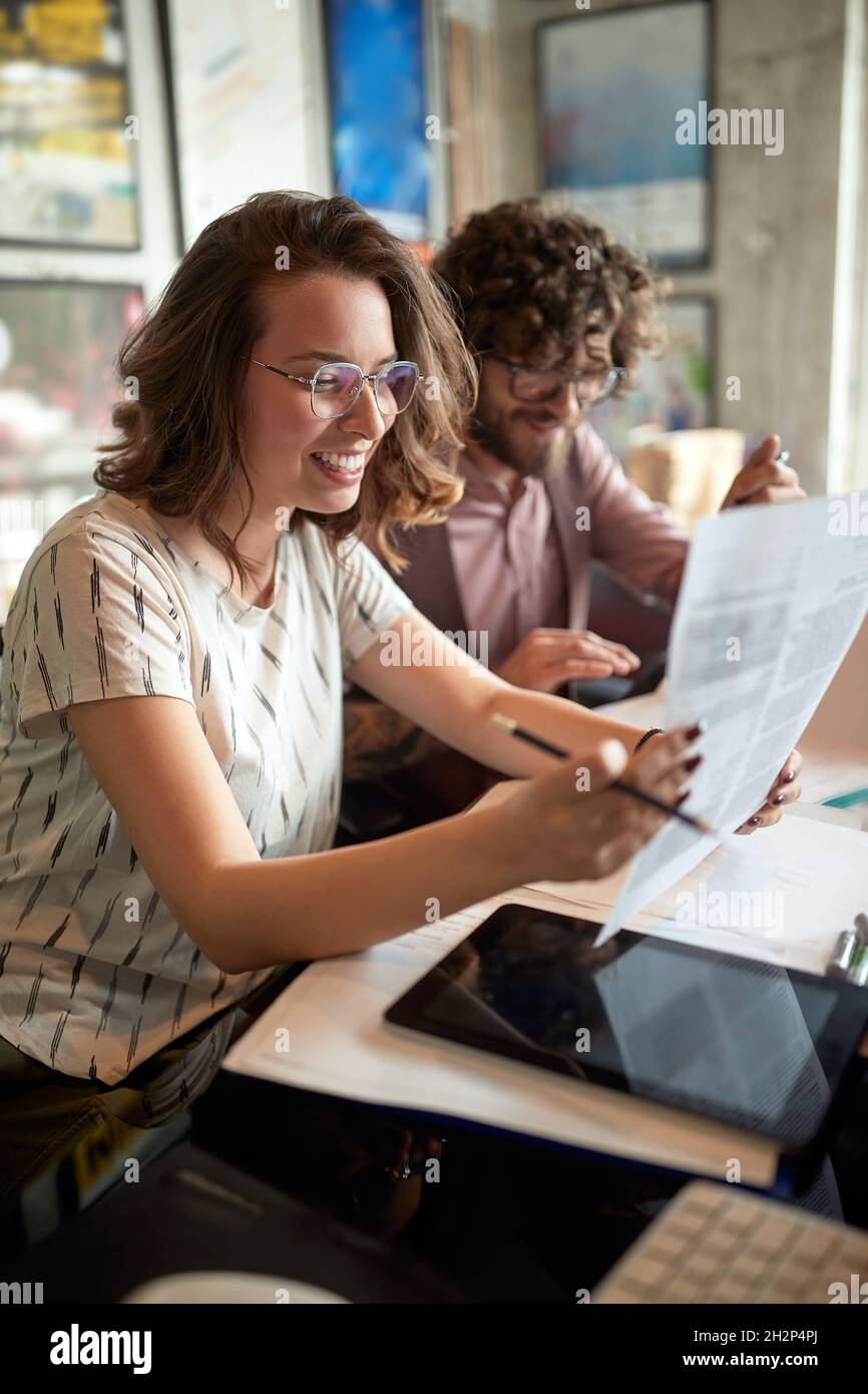 femme caucasienne tenant du papier, lisant, souriant, assise à côté d'un collègue de sexe masculin au bureau. Banque D'Images