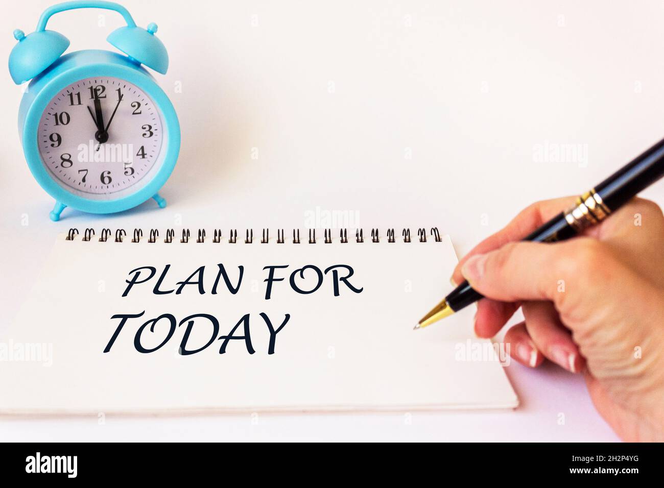 PLAN POUR AUJOURD'HUI, le texte est écrit sur un bloc-notes par la main d'une femme, sur un fond blanc.Il y a un réveil à proximité Banque D'Images