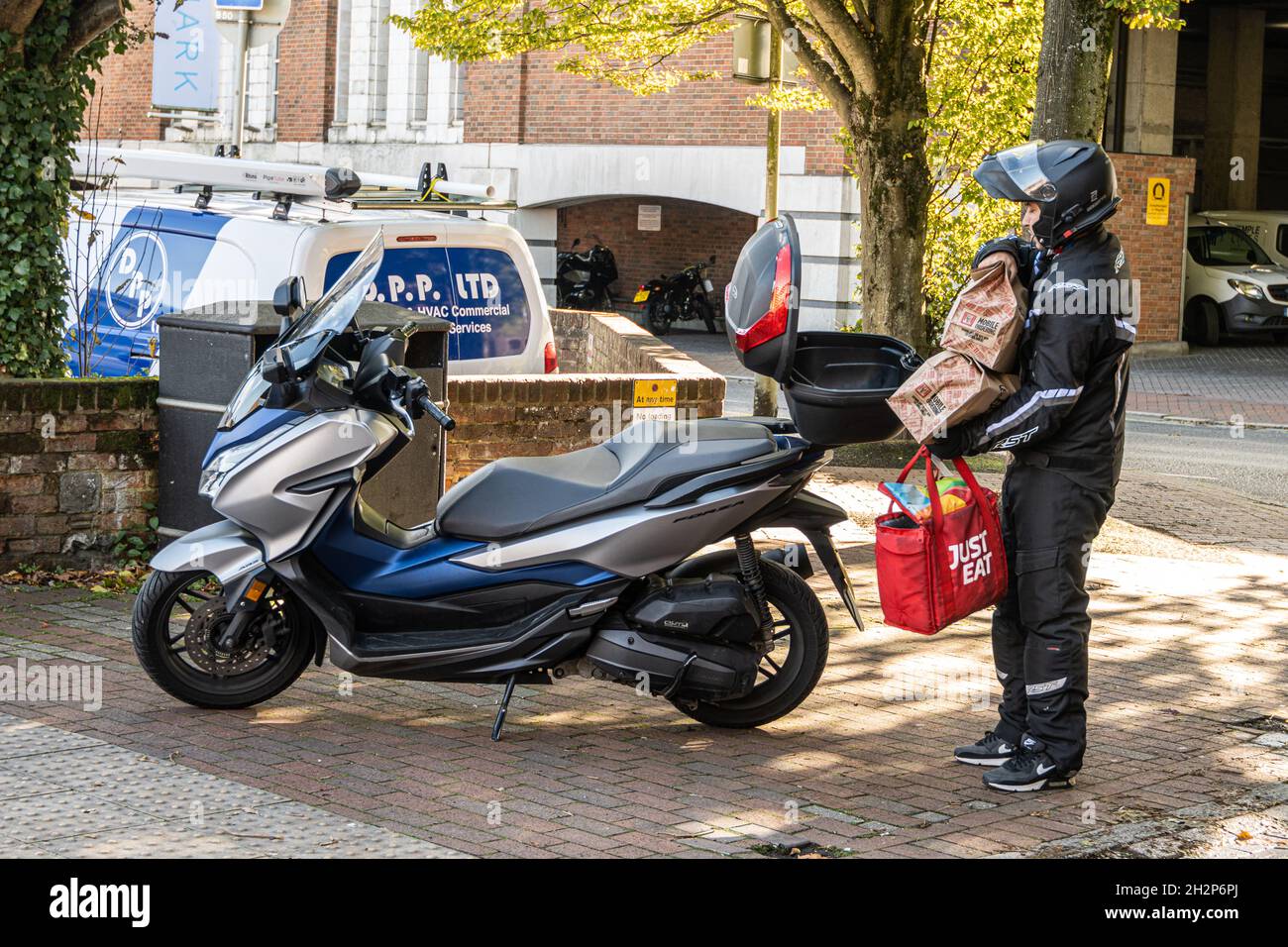 Livrant de la nourriture à emporter, Un chauffeur de livraison juste manger transporte les commandes à sa moto.Winchester, Hampshire, Royaume-Uni Banque D'Images