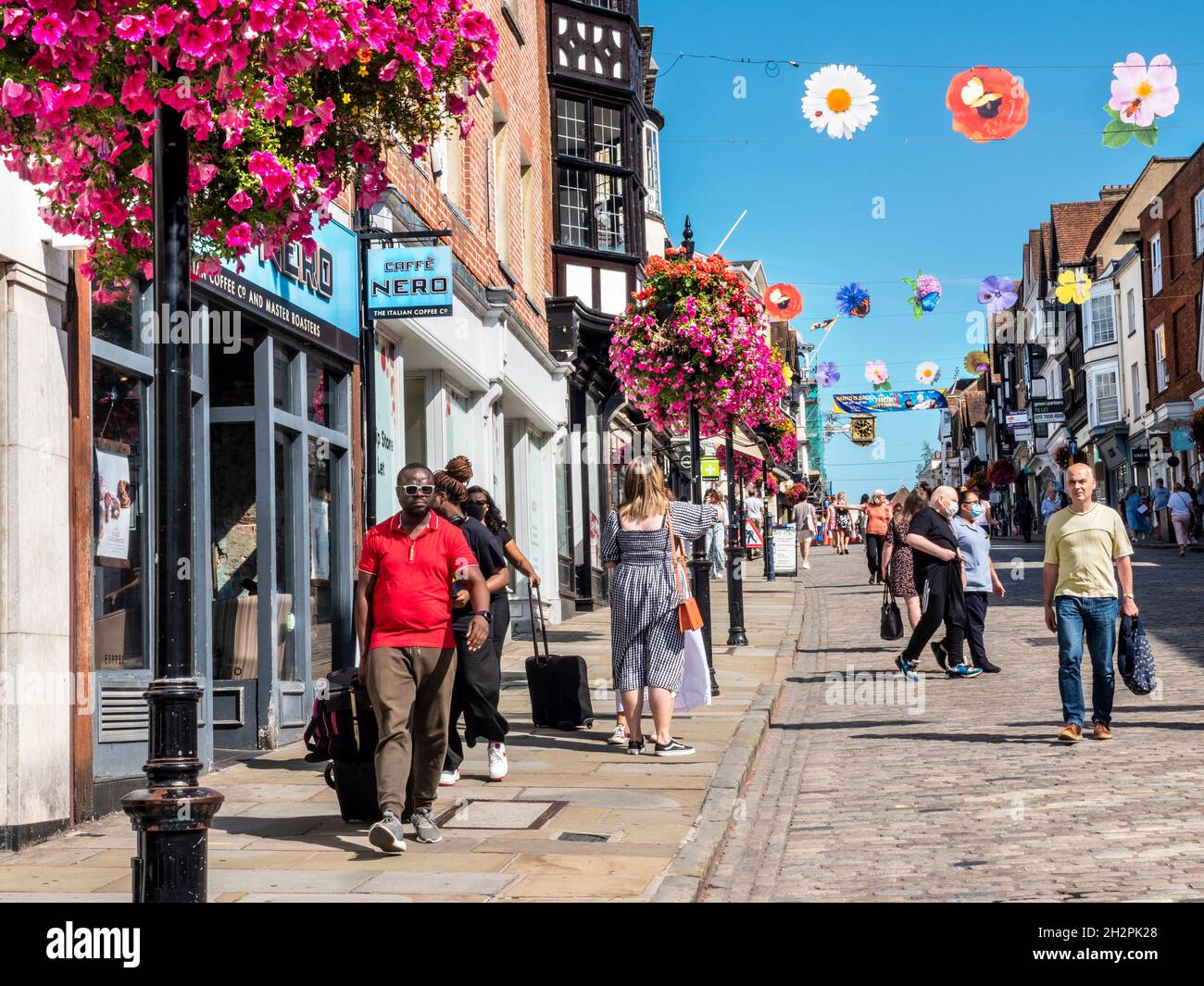 Guildford High Street fait des boutiques avec des acheteurs, certains portant des masques covid.Paniers à fleurs d'automne et bannières saisonnières colorées au soleil bleu clair et chaud Banque D'Images