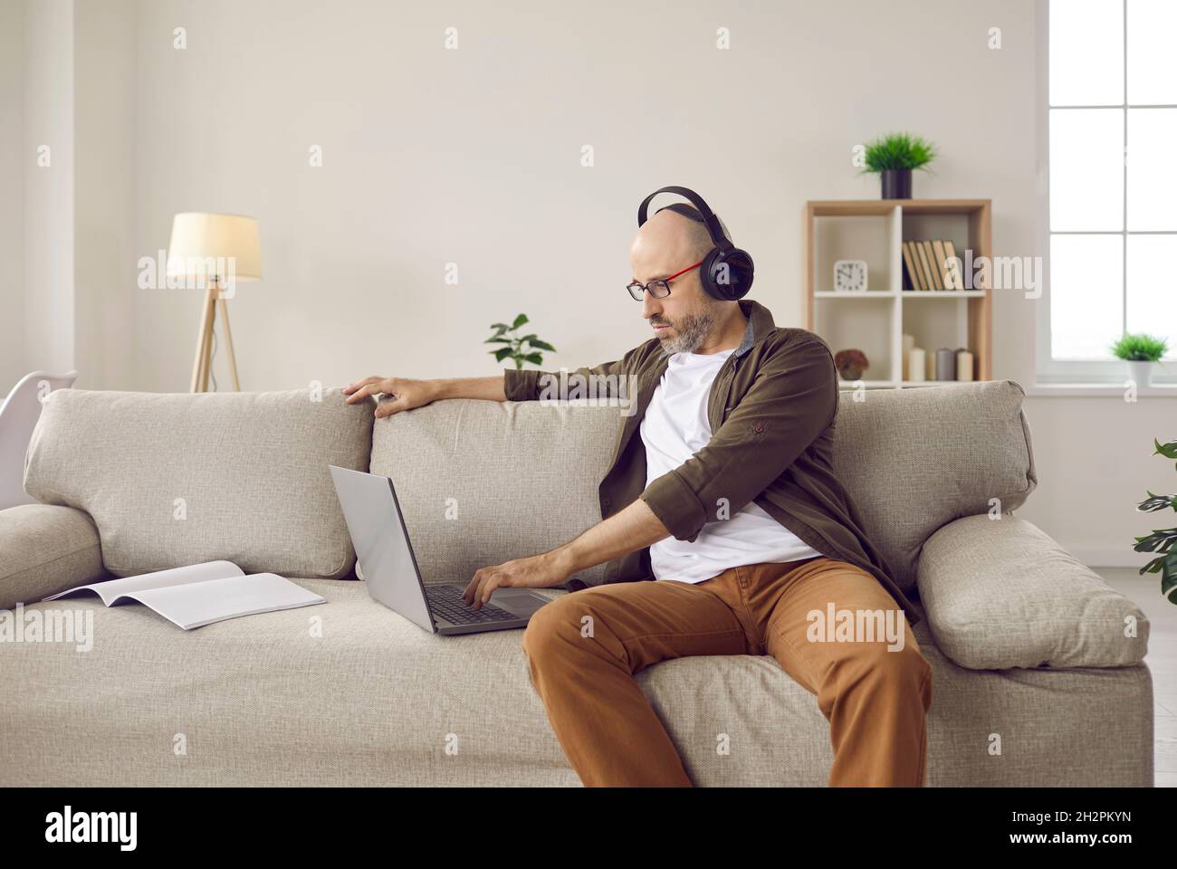 Adulte homme détendu écoutant de la musique avec un casque tout en travaillant sur un ordinateur portable à la maison. Banque D'Images