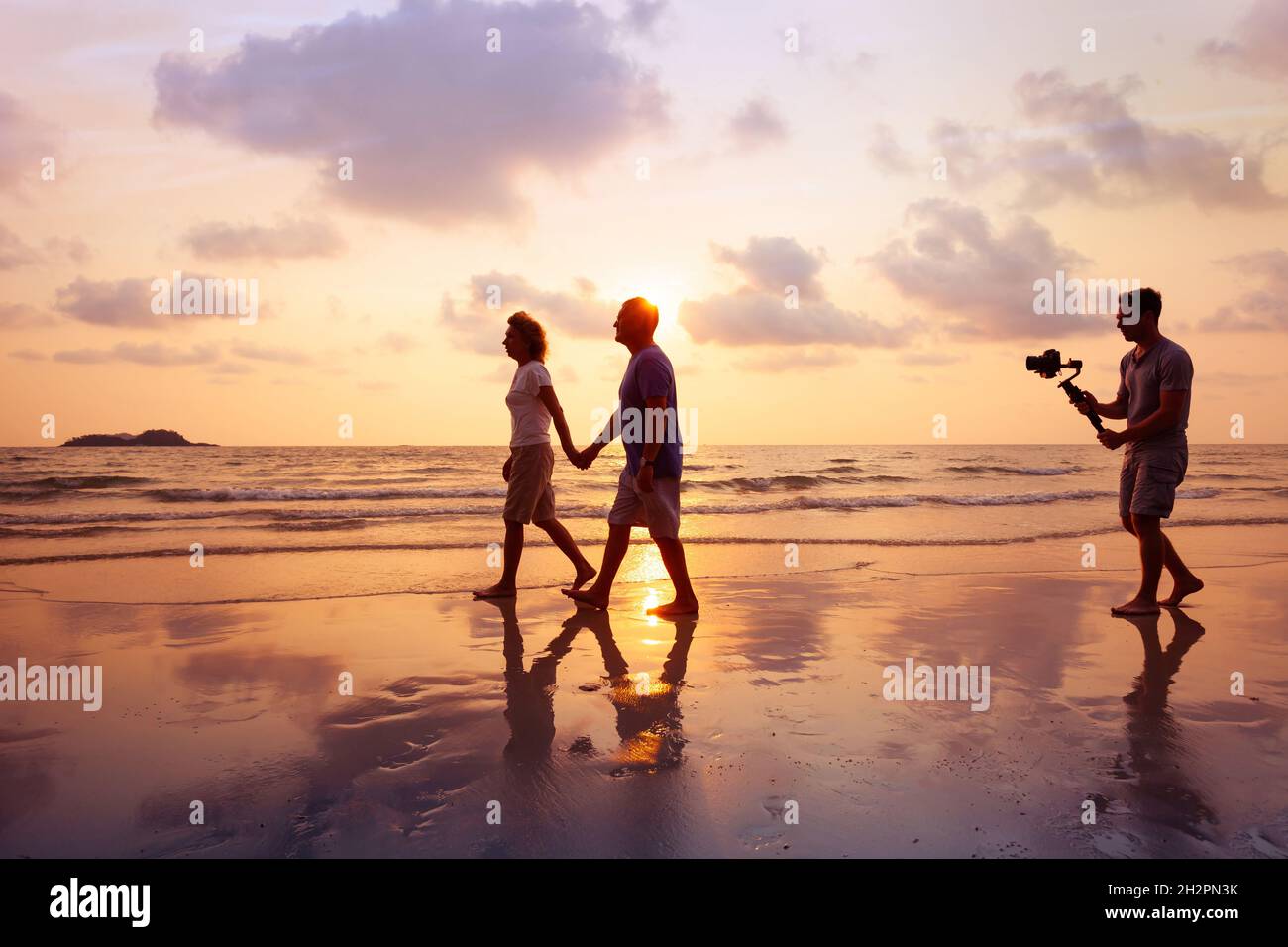 réalisateur filmant vidéo de couple avec stabilisateur de caméra sur la plage au coucher du soleil, vidéaste professionnel travaillant sur le film Banque D'Images