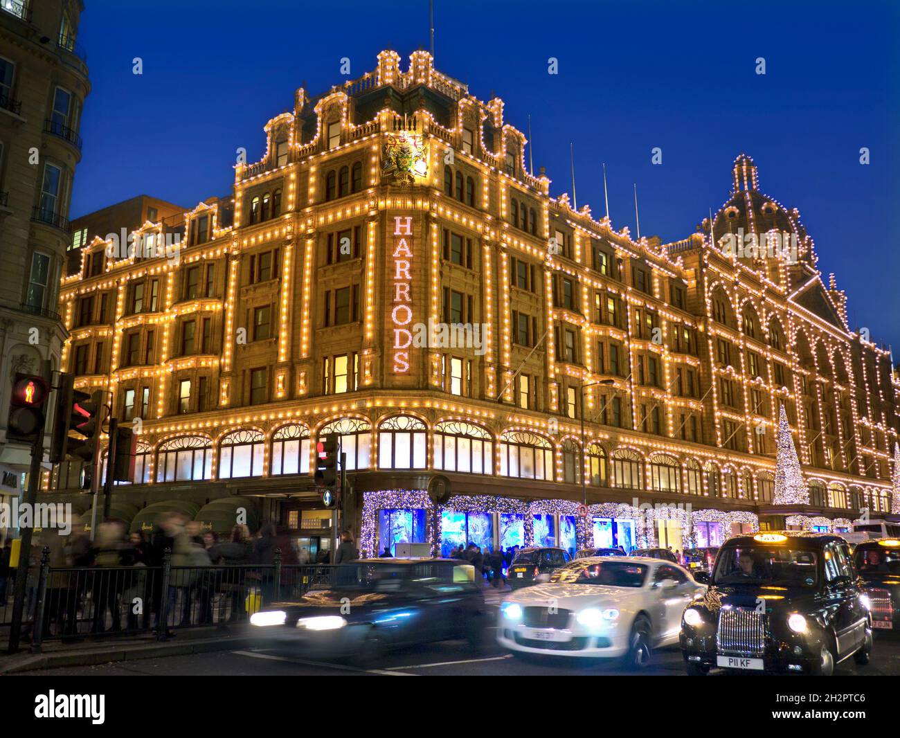 HARRODS NUIT NOËL SHOPPERS FLOU LA CIRCULATION Harrods grand magasin au crépuscule avec les lumières de Noël shoppers et passer le trafic flou Knightsbridge Londres SW1 Banque D'Images