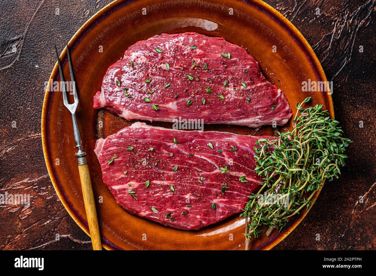 Steak de calotte cru ou steak d'aloyau dans une assiette rustique au thym et à l'huile d'olive. Arrière-plan sombre. Vue de dessus Banque D'Images