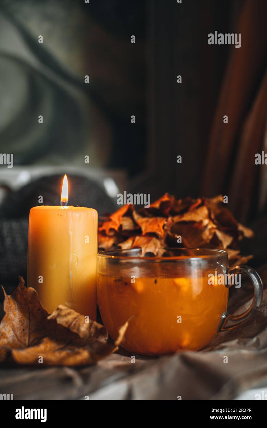 Bougie brûlante et une grande tasse de thé d'argousier orange chaud dans une maison confortable soirée d'automne encore la vie avec des feuilles sèches. Banque D'Images