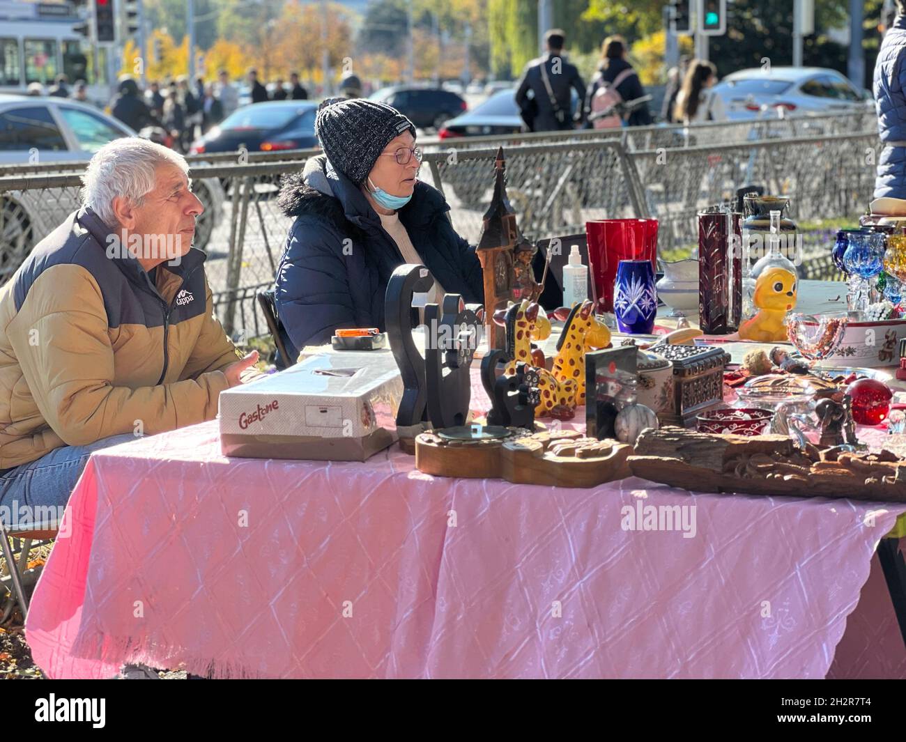 Un couple d'âge moyen assis dans la stalle de leur marché aux puces.Leur marchandise est exposée sur une table basse et ils attendent les clients. Banque D'Images