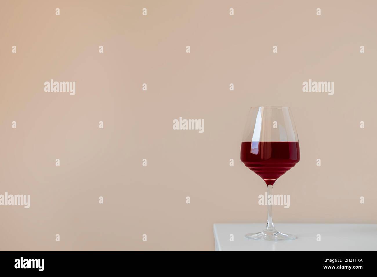 Verre de vin rouge sur table blanche sur fond beige neutre avec espace pour le texte, composition simple et élégante Banque D'Images