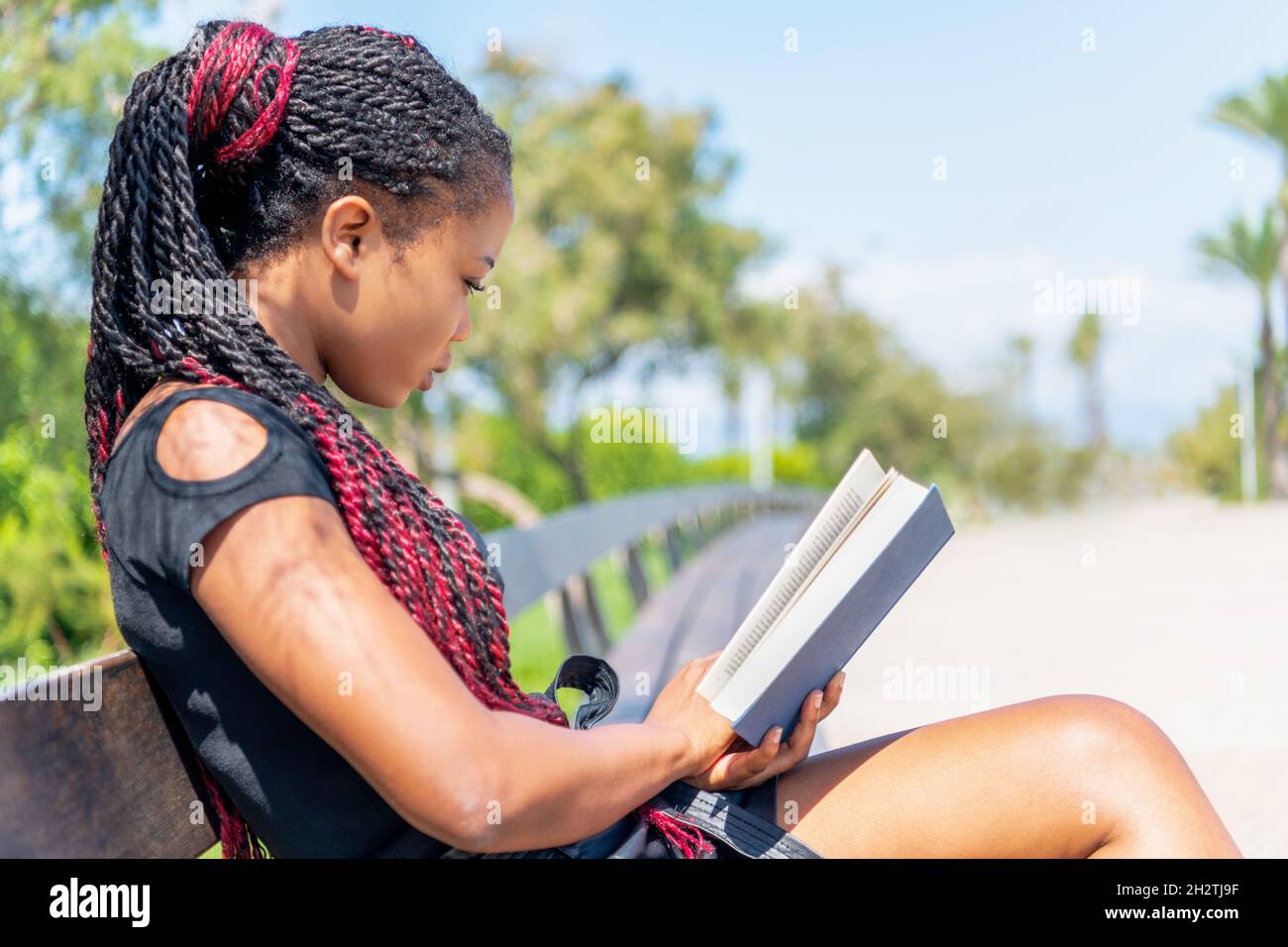 Étudiant africain lisant assis sur un banc à l'extérieur dans un jour ensoleillé Banque D'Images