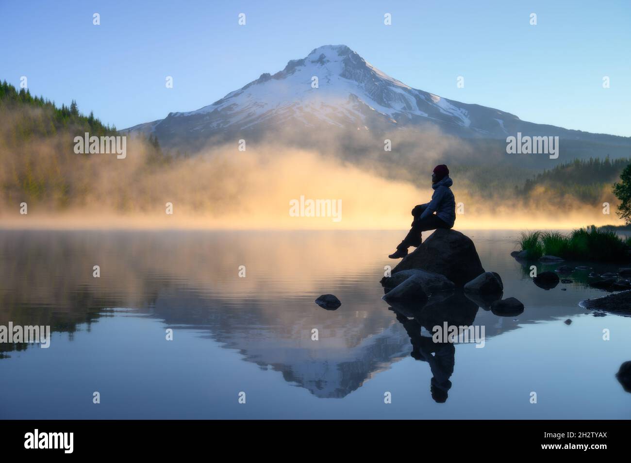 Voyageur assis sur le rocher et regardant la vue panoramique de Mount Hood avec le lever du soleil au lac Trillium, Oregon Banque D'Images