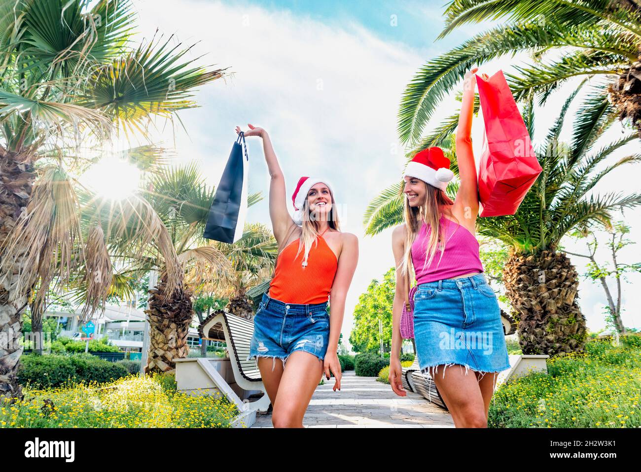 joyeux noël !Jeunes sœurs adultes célébrant Noël porter un chapeau de père noël marchant palmiers arbres rue faisant du shopping pendant les vacances chaudes d'hiver. Banque D'Images