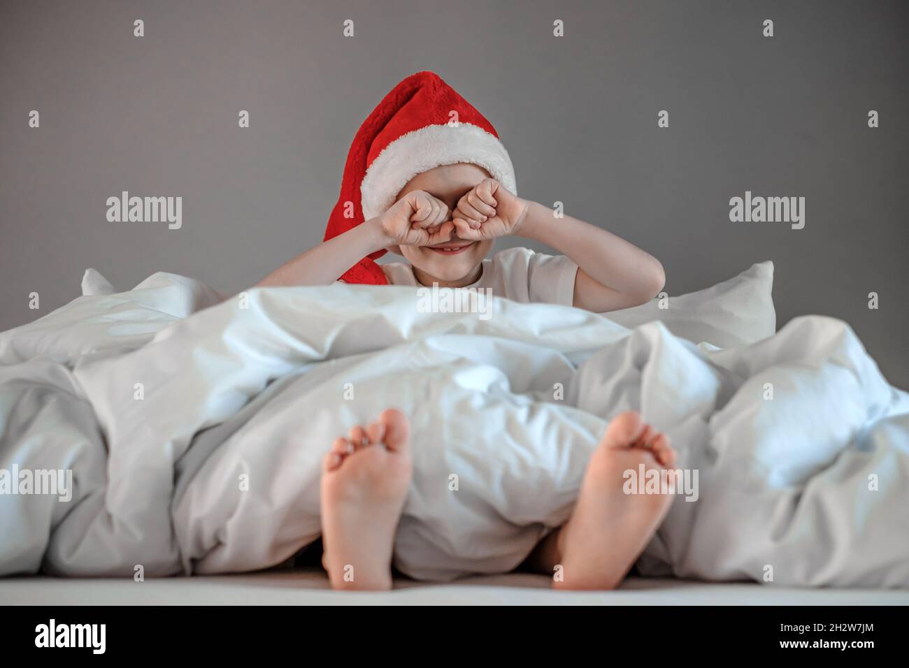 Drôle de garçon mignon se réveiller et de pleurs yeux dans un chapeau de père Noël.Joyeuses vacances.Concept du matin de Noël.Photo de haute qualité Banque D'Images