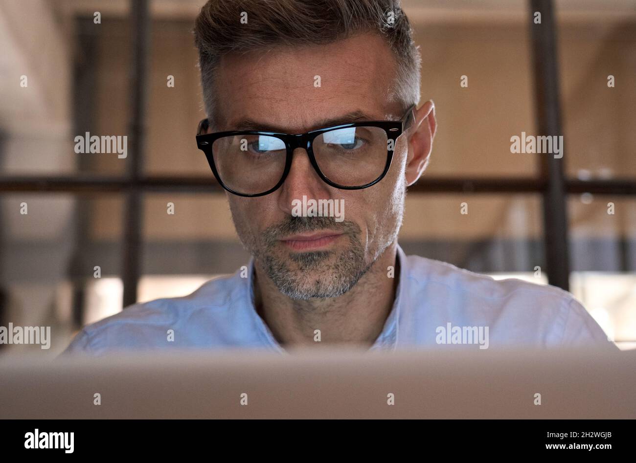 Homme d'affaires concentré regardant l'écran d'ordinateur réfléchissant dans des lunettes. Banque D'Images
