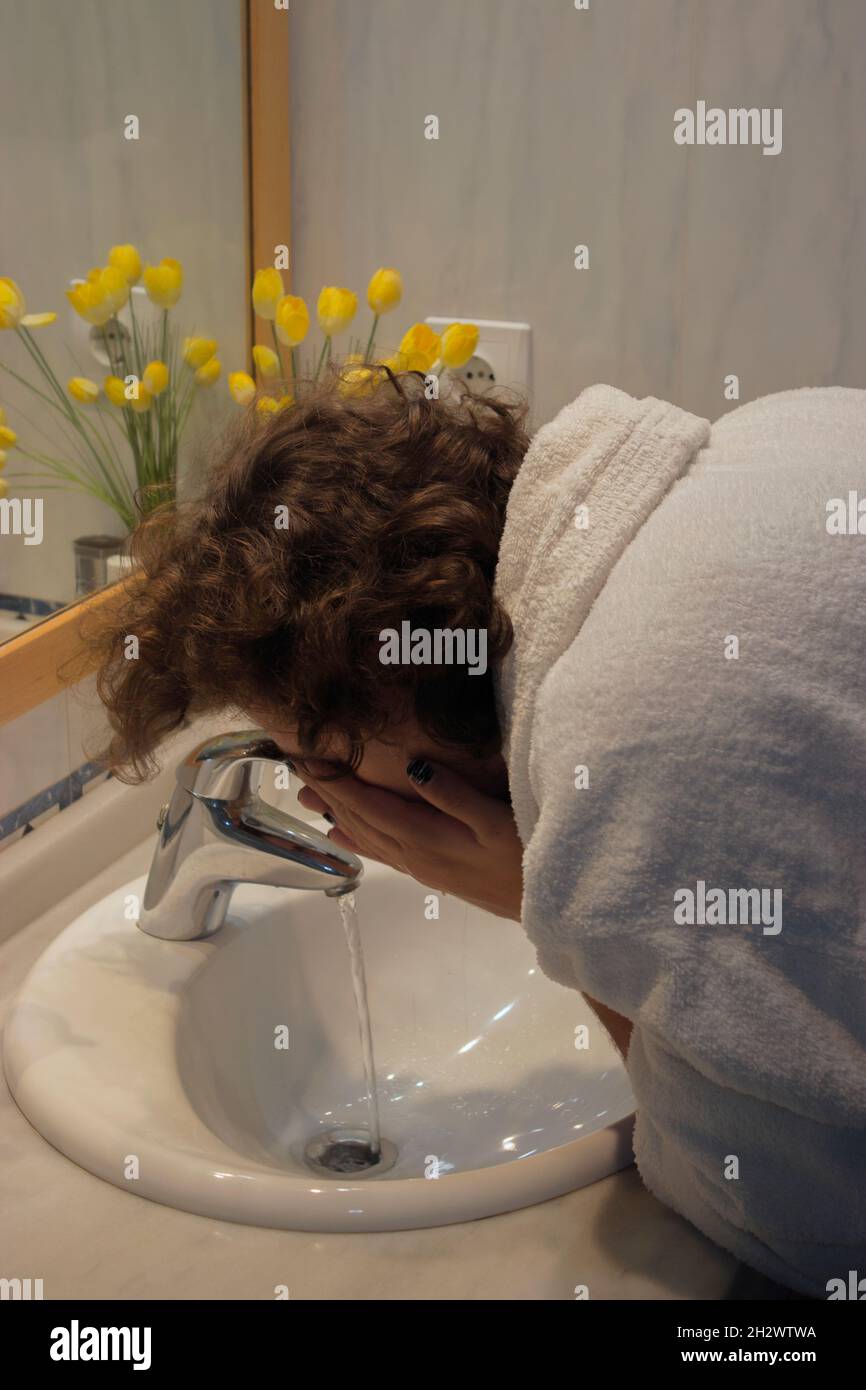 Un jeune homme en peignoir lave son visage dans son lavabo avant de se raser.Home Spa concept Beauté concept. Banque D'Images