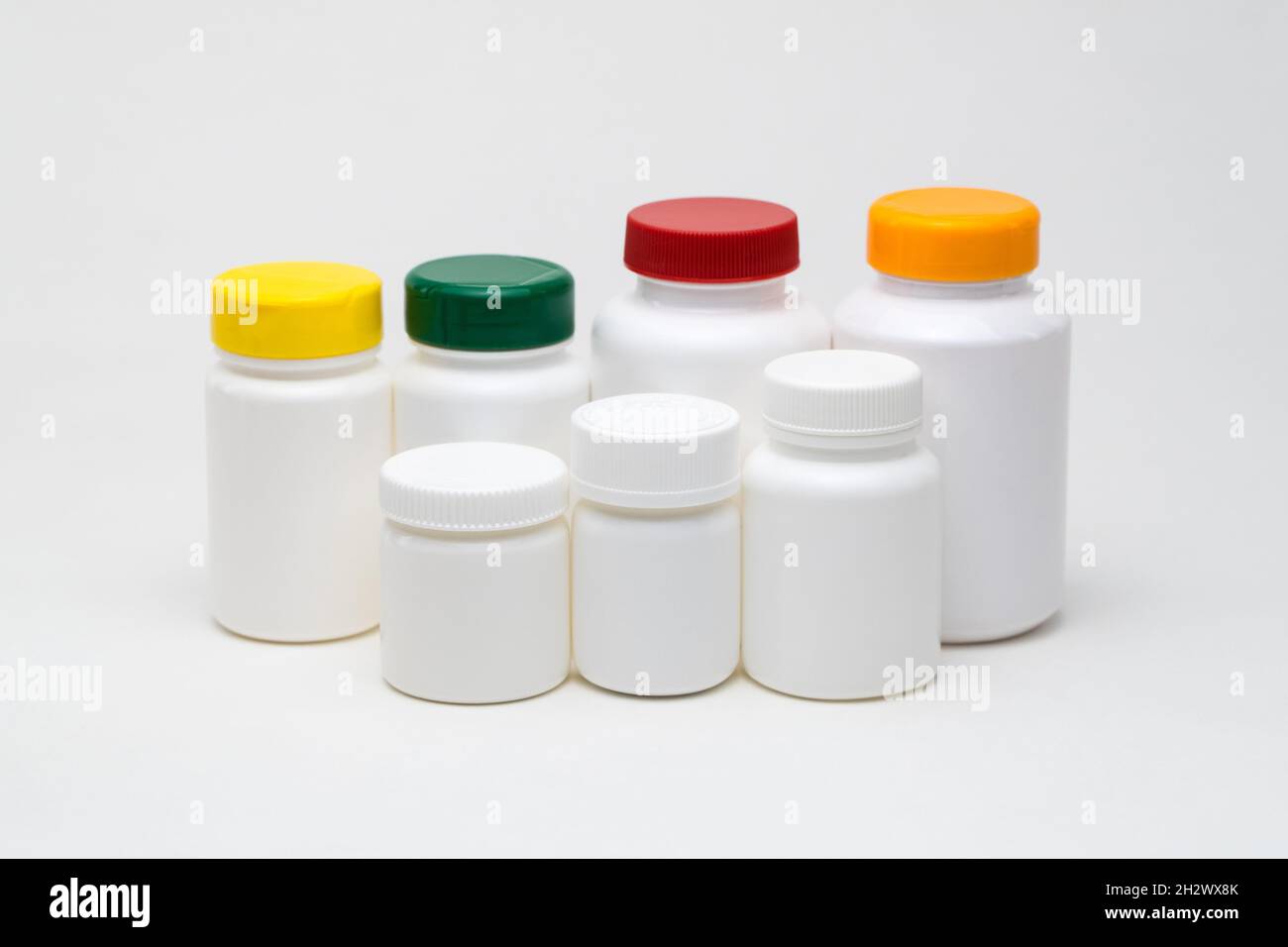 Pots de pilules en plastique blanc sur fond blanc.Couvercles multicolores.Isolé Banque D'Images