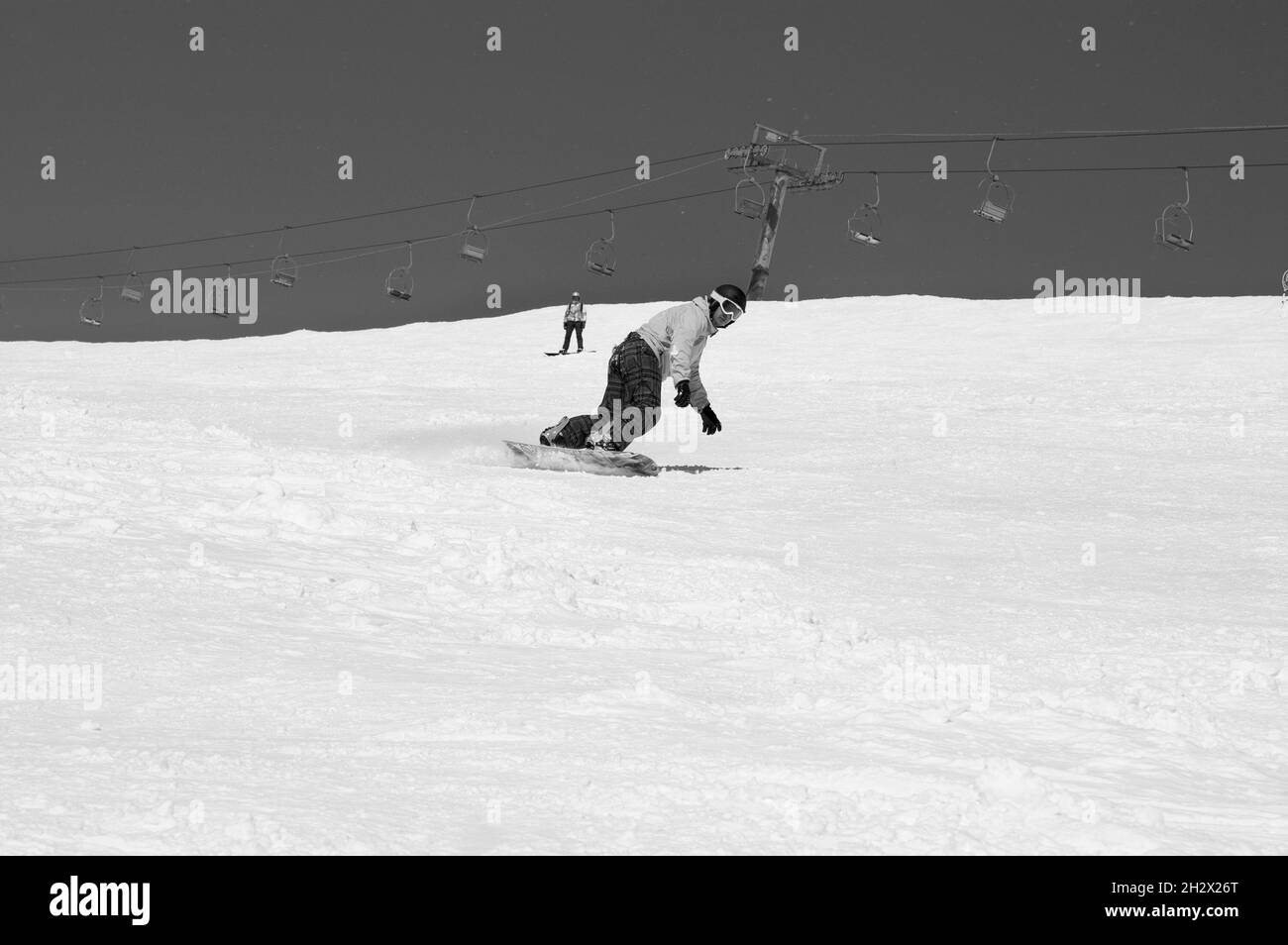 La snowboardeuse descend sur une piste de ski enneigée dans les montagnes d'hiver par beau temps.Télésiège et ciel avec neige en arrière-plan.Caucase montagnes, région Dombay Banque D'Images